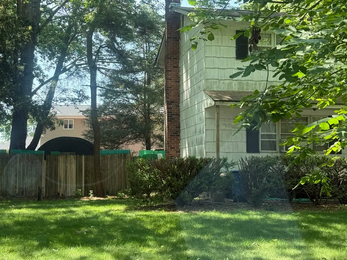 Downsizing or retiring in Patchogue: two-story house with dark shutters behind a wood fence and shade trees